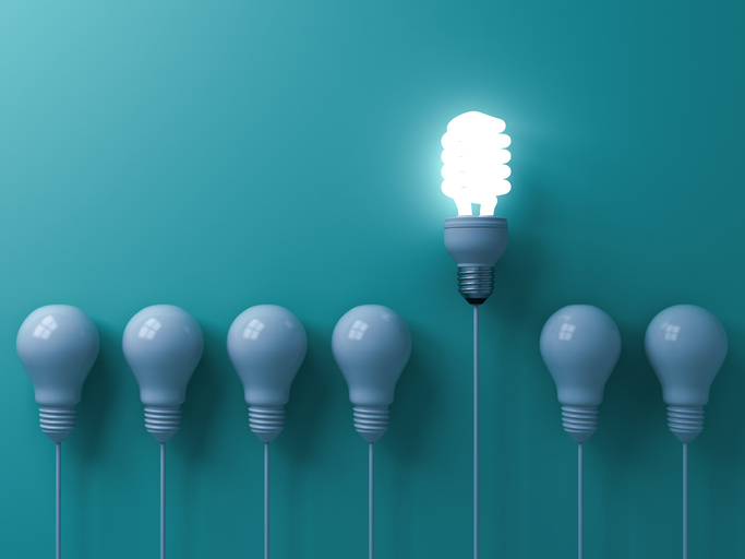 One eco energy saving light bulb glowing and standing out from unlit incandescent white bulbs on green pastel color wall background leadership and different creative idea concepts 3D rendering